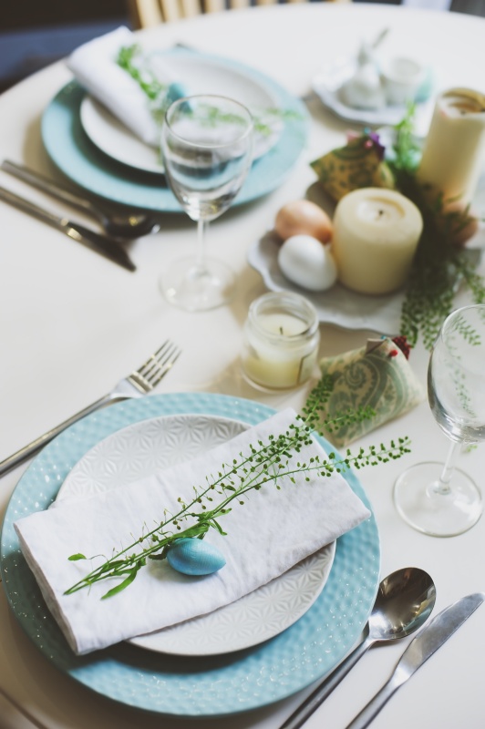 Easter and spring festive table decorated in blue and white tones in natural rustic style, with eggs, bunny, fresh flowers and candles.