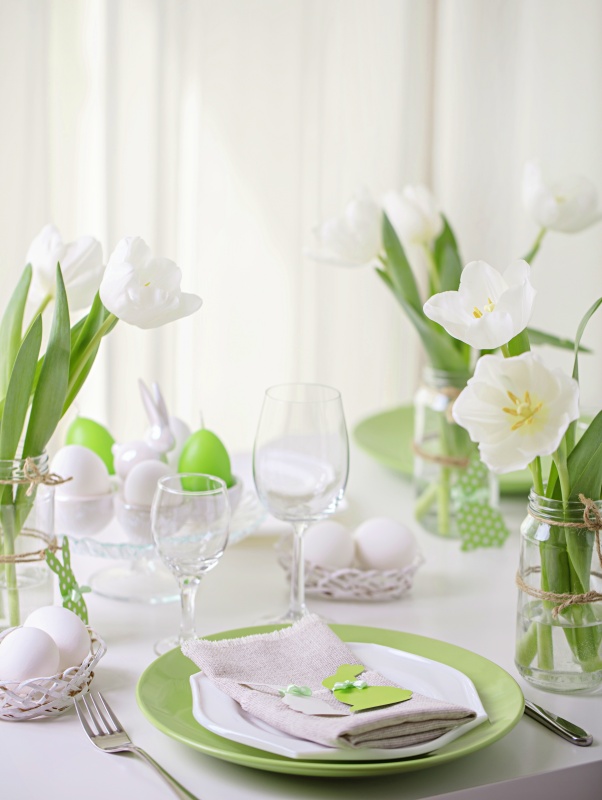 Decor and table setting of the Easter table is a vase with white tulips and dishes of green and white color. Easter decor with white polka dots. 