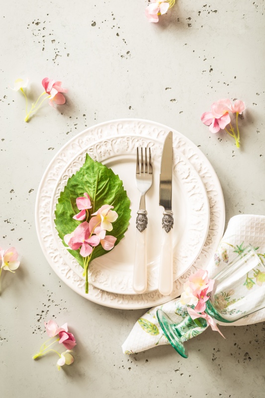 Easter, spring or summer table setting design captured from above (top view, flat lay). Ornamental white plates, glass, cutlery and pink flowers. 