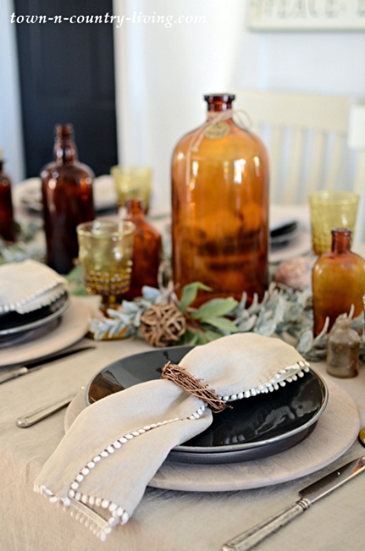 Linen pom pom napkins and vintage amber bottles at a table setting