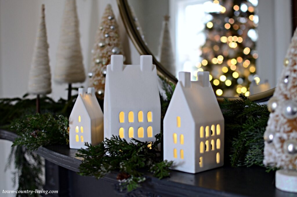 White Ceramic Light-Up Houses and Christmas Greenery on a Black Vintage Mantel