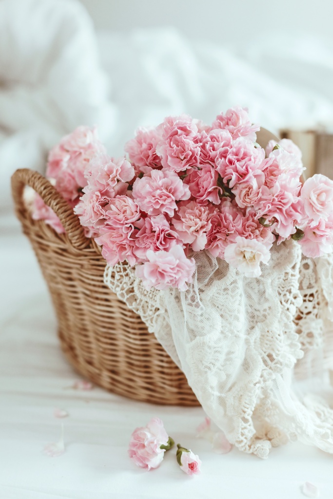 Shabby chic style. Pink pastel flowers in wicker basket on the bed.