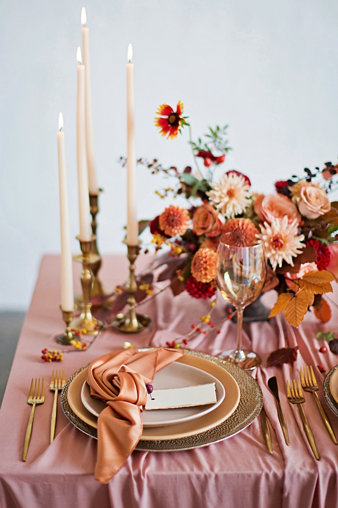 Beautiful table setting with autumn flowers, orange and pink napkins and burning candles. 