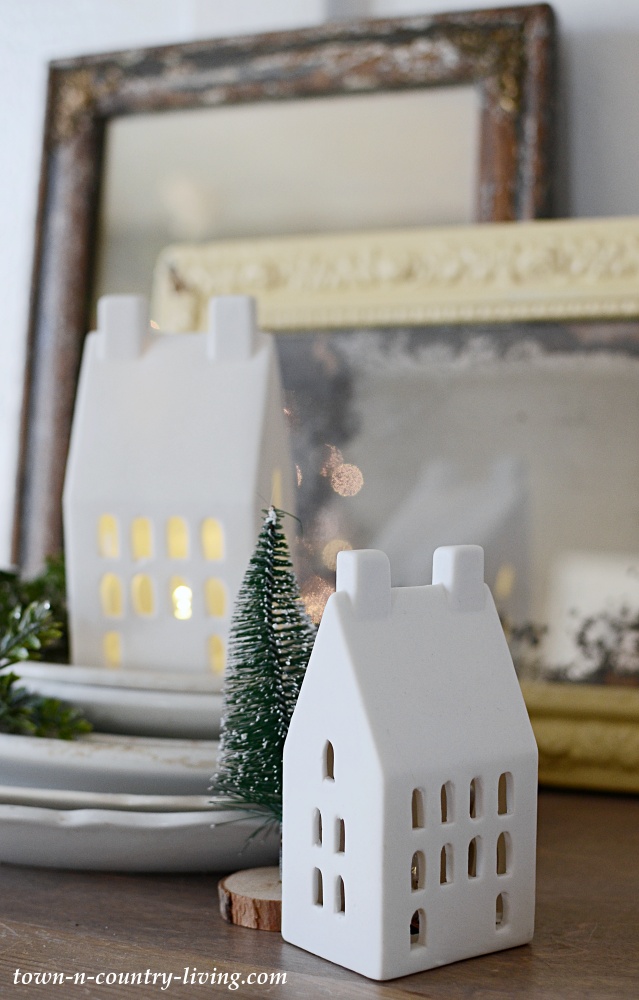Light-up ceramic Christmas houses with a stack of white ironstone plates
