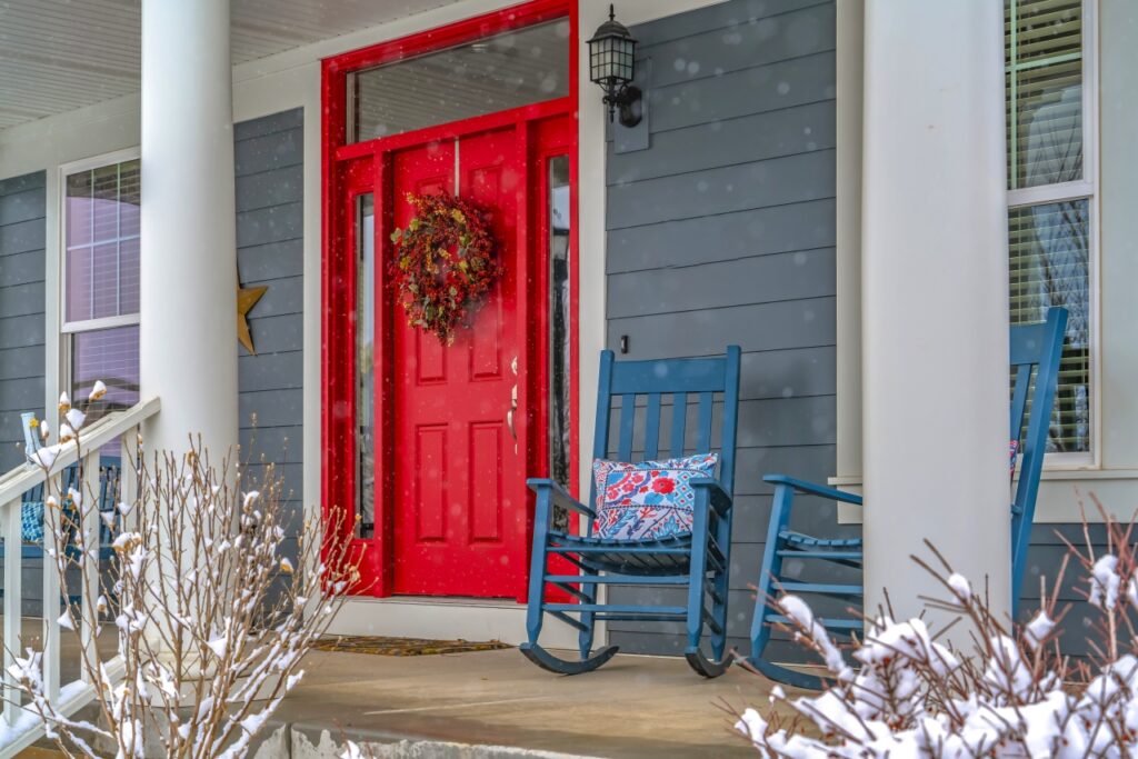 Gray house with red door, rocking chair, and Christmas wreath