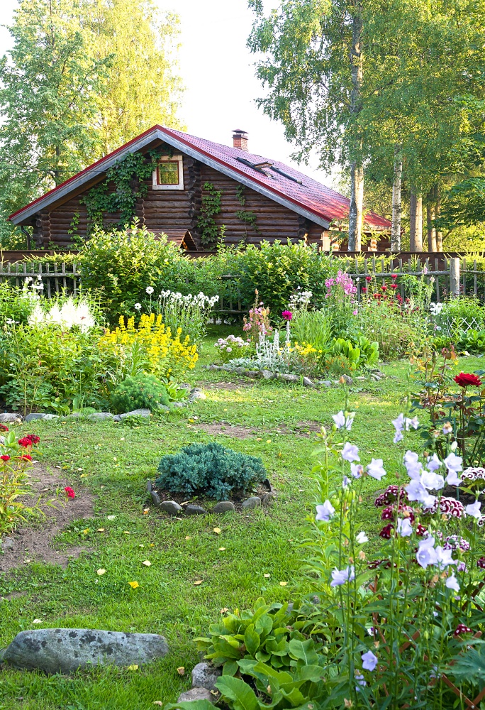 Country house made of dark logs and beautiful garden with flowers