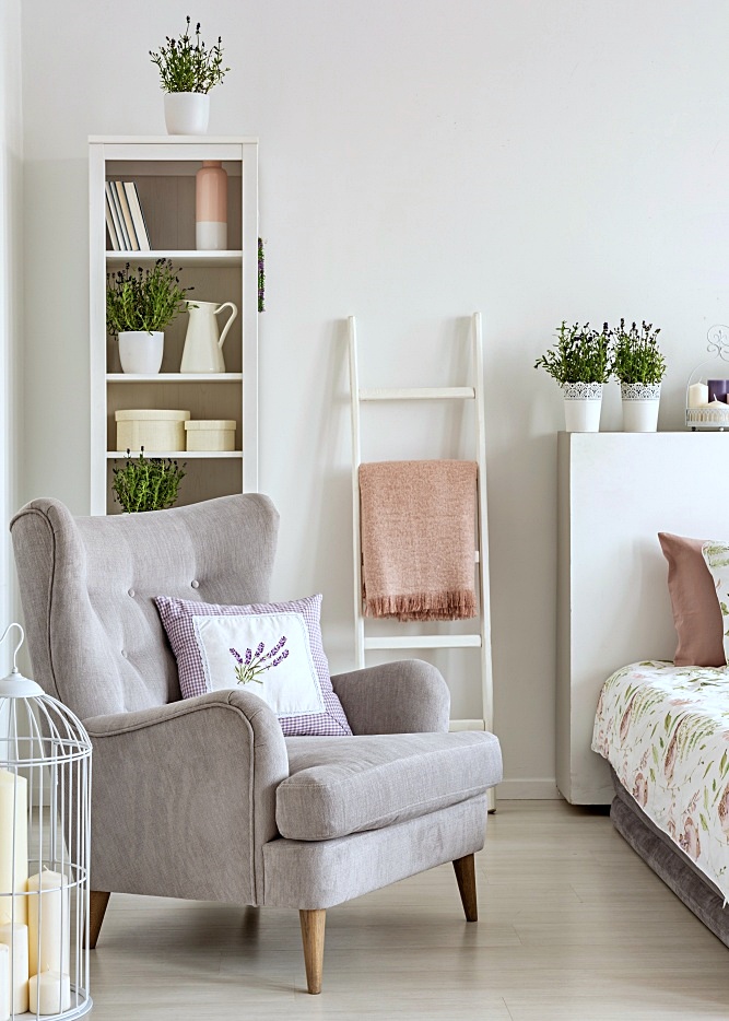 Grey armchair with a pillow, ladder with a blanket and shelf in a feminine bedroom