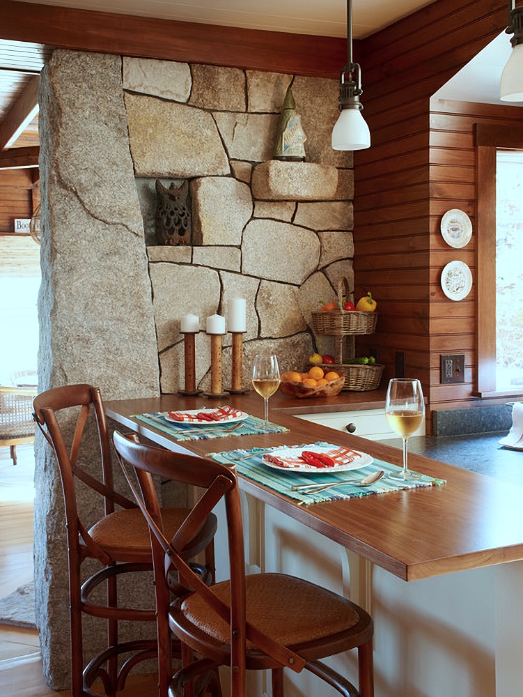 Stone wall next to breakfast bar with cross back stools