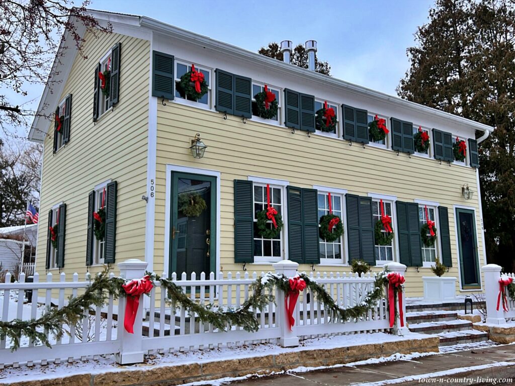 Yellow clapboard house with white picket fence - decorated with wreaths and garlands for Christmas
