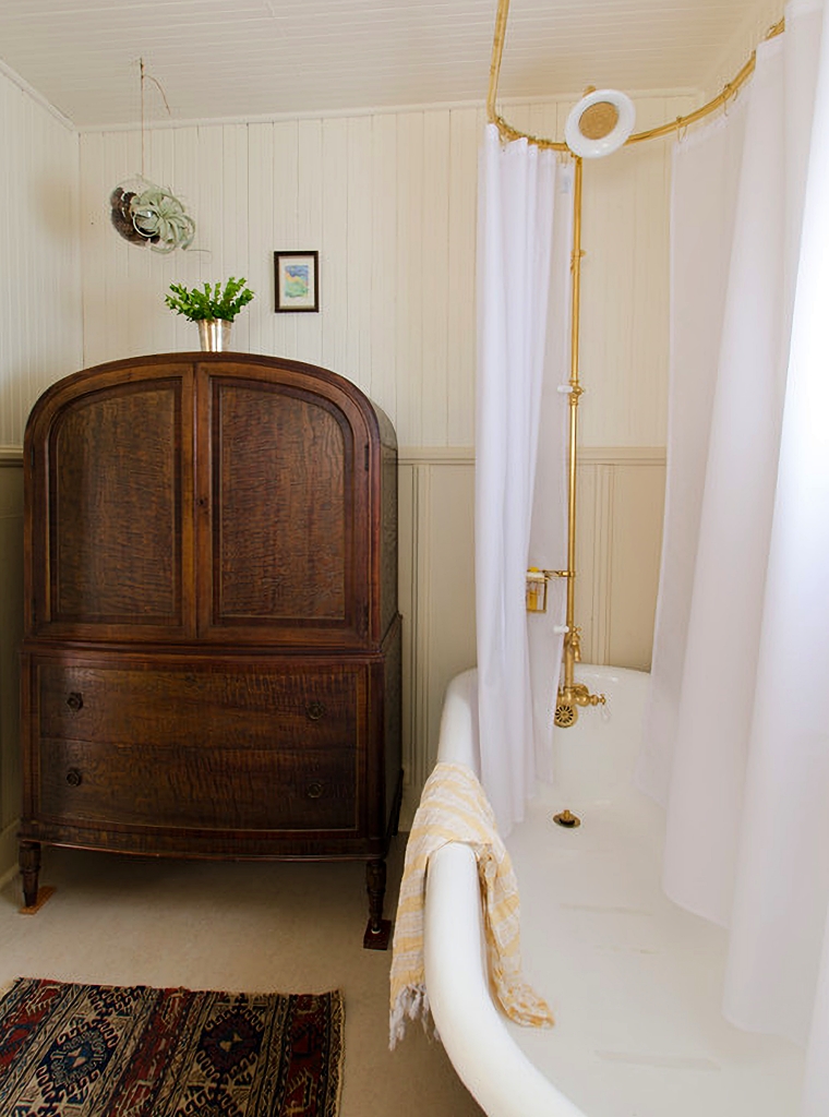 arched wood armoire next to claw foot tub